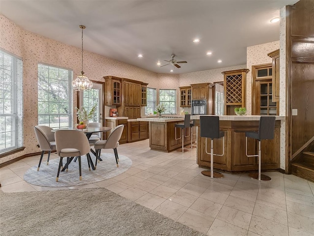 3601 Rena Dawn Ln, Edmond, OK 73013 - kitchen featuring black oven, a kitchen island, a breakfast bar area, wallpapered walls, and brown cabinets