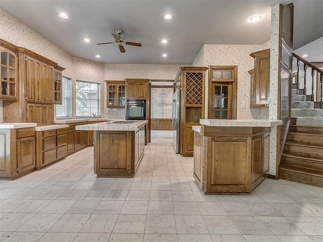 3601 Rena Dawn Ln, Edmond, OK 73013 - kitchen with tile countertops, a center island, stainless steel refrigerator, black oven, and wallpapered walls