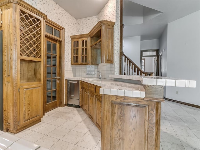 3601 Rena Dawn Ln, Edmond, OK 73013 - kitchen with dishwasher, tile counters, brown cabinetry, a peninsula, and wallpapered walls