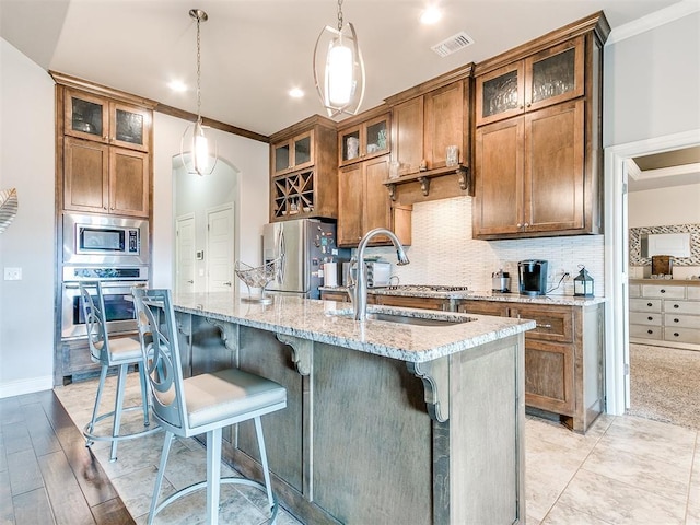 kitchen with a kitchen island with sink, visible vents, crown molding, appliances with stainless steel finishes, and brown cabinets