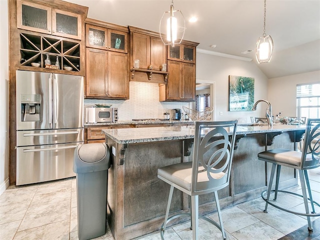 kitchen featuring brown cabinets, a sink, stainless steel appliances, decorative backsplash, and a center island with sink