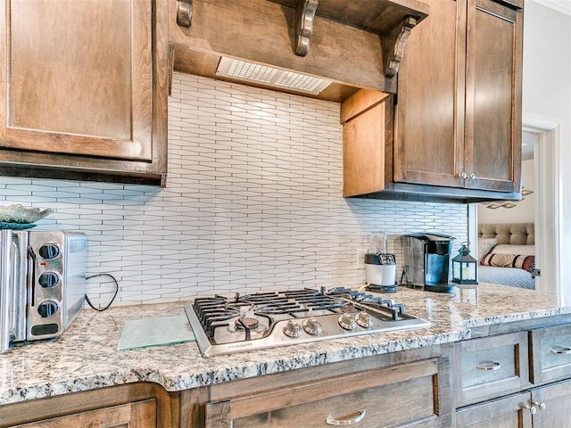 kitchen featuring decorative backsplash, ventilation hood, light stone countertops, and stainless steel gas stovetop