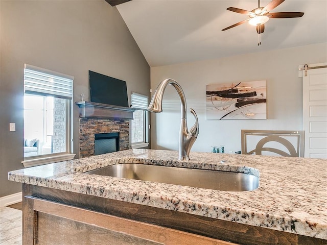 room details with baseboards, ceiling fan, a stone fireplace, and a sink