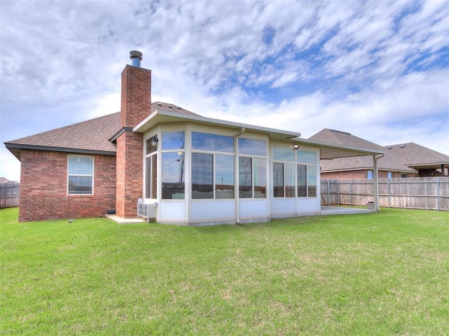 rear view of property with fence, a chimney, a sunroom, brick siding, and a yard