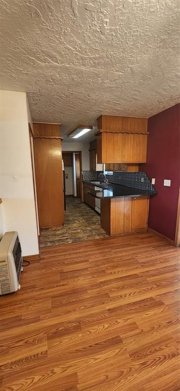 kitchen with brown cabinetry, dark countertops, a peninsula, and wood finished floors