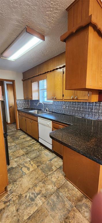 kitchen with brown cabinets, tasteful backsplash, a sink, stone finish flooring, and white dishwasher