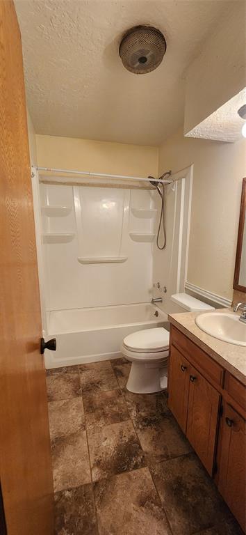 bathroom with stone finish flooring, toilet, tub / shower combination, and vanity