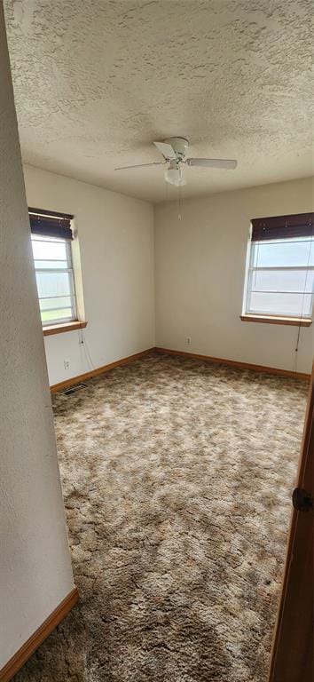 empty room featuring a textured ceiling, plenty of natural light, and baseboards