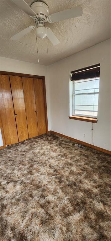 unfurnished bedroom featuring a textured ceiling, carpet flooring, baseboards, a closet, and a ceiling fan