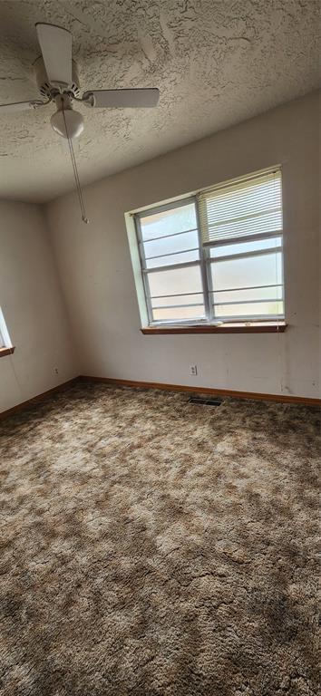 carpeted spare room featuring a textured ceiling, a ceiling fan, and baseboards