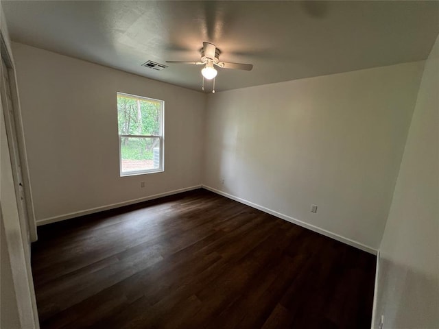 unfurnished room featuring dark wood-style floors, a ceiling fan, visible vents, and baseboards