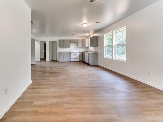 1823 E Rutgers Ave, Guthrie, OK 73044 - unfurnished living room featuring a ceiling fan, baseboards, a sink, and light wood finished floors