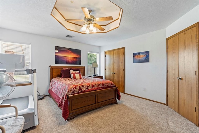 bedroom with visible vents, two closets, light carpet, a ceiling fan, and baseboards