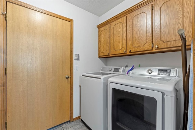 clothes washing area featuring light tile patterned floors, washer and dryer, and cabinet space
