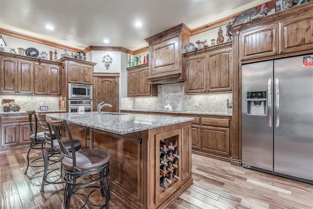 1400 S May Ave, Guthrie, OK 73044 - kitchen with stainless steel appliances, a sink, decorative backsplash, a kitchen breakfast bar, and light wood-style floors