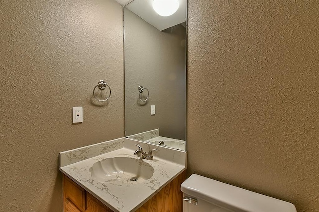 bathroom with vanity, toilet, and a textured wall