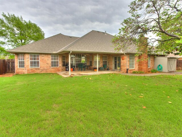 rear view of house with brick siding, roof with shingles, fence, and a yard