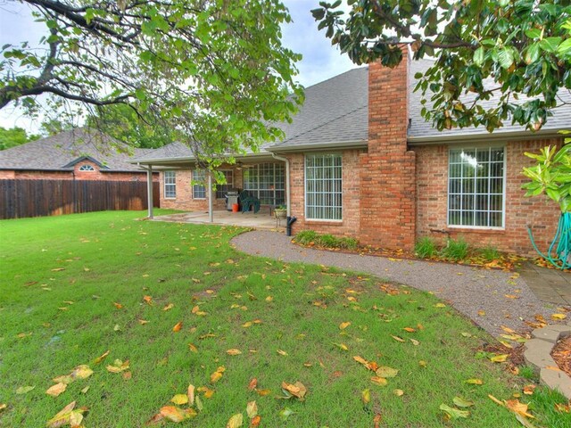 exterior space featuring a chimney, a lawn, a patio area, brick siding, and fence