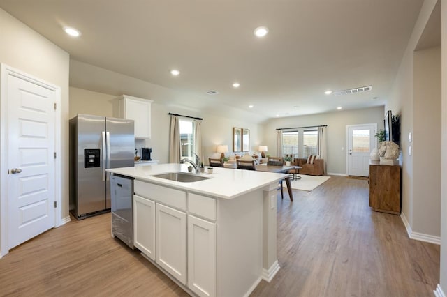 kitchen with light wood finished floors, a sink, stainless steel appliances, white cabinetry, and open floor plan