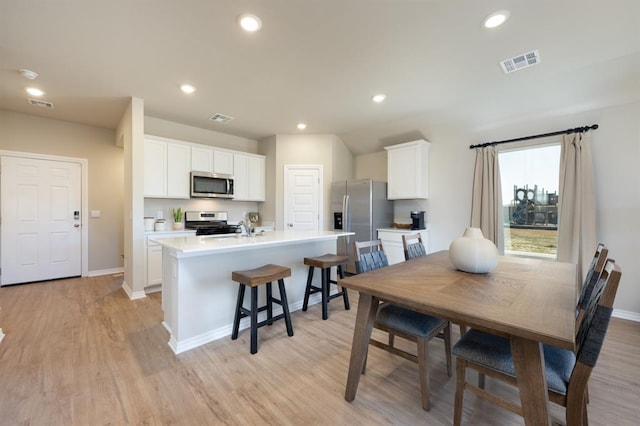 kitchen with visible vents, baseboards, white cabinets, appliances with stainless steel finishes, and an island with sink