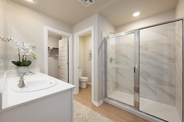 bathroom with wood finished floors, toilet, a sink, visible vents, and a stall shower