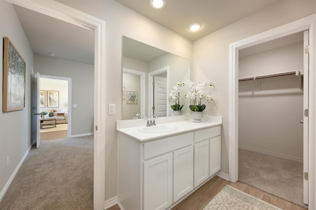 bathroom with wood finished floors, a walk in closet, vanity, and baseboards