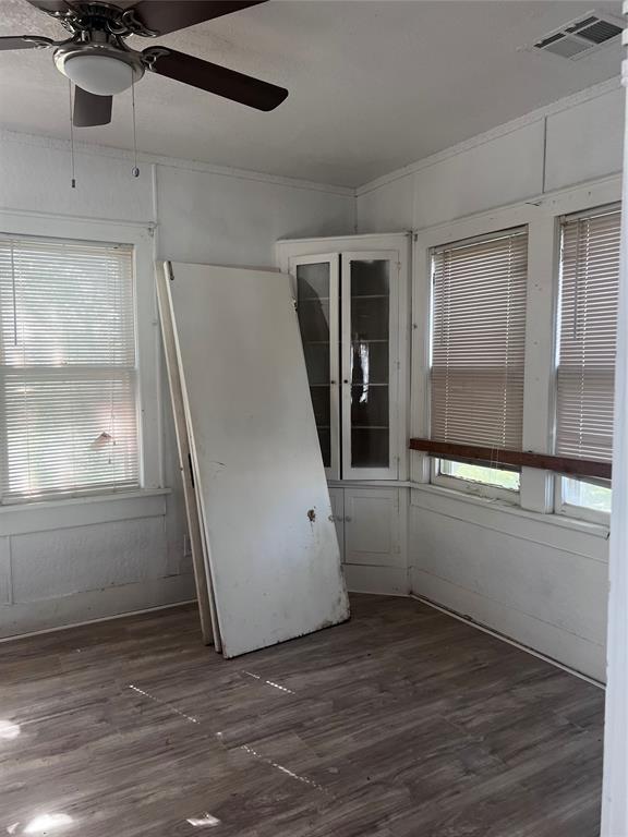 spare room featuring wood finished floors, visible vents, a ceiling fan, and ornamental molding