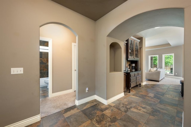hallway featuring baseboards, arched walkways, and stone tile flooring