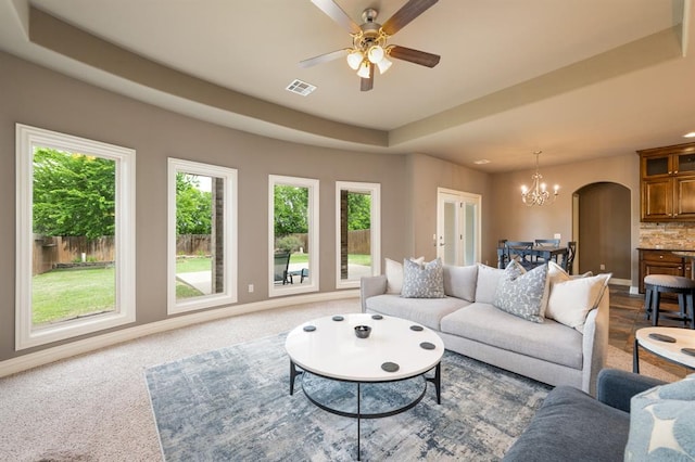 living room featuring arched walkways, visible vents, a healthy amount of sunlight, and ceiling fan with notable chandelier