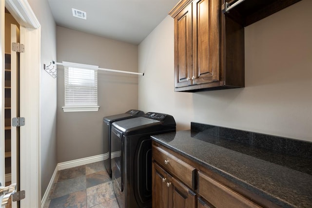washroom featuring visible vents, baseboards, stone finish floor, washer and clothes dryer, and cabinet space