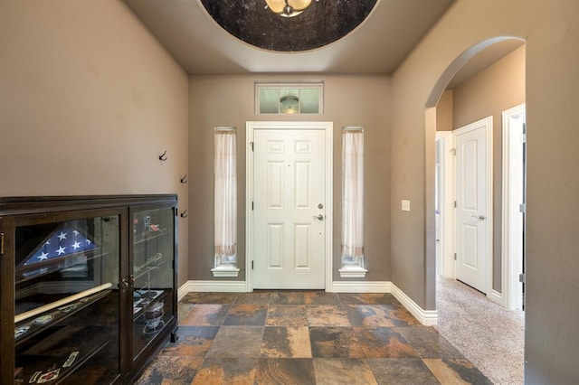 foyer entrance with arched walkways, baseboards, and stone finish flooring