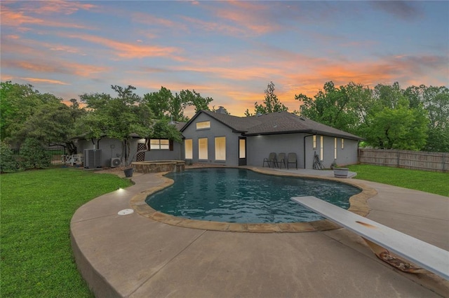 pool at dusk with a diving board, a patio area, a fenced in pool, a fenced backyard, and a yard