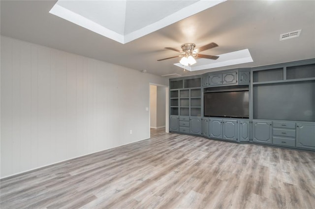 unfurnished living room featuring a ceiling fan, a skylight, visible vents, and light wood finished floors