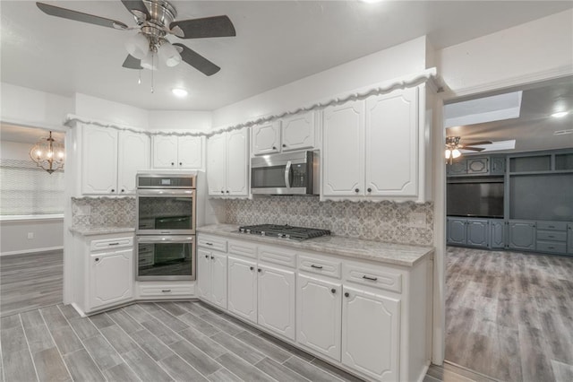 kitchen featuring decorative backsplash, white cabinetry, ceiling fan with notable chandelier, stainless steel appliances, and light wood-style flooring