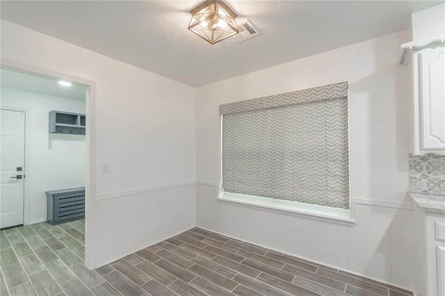 unfurnished dining area with wood finished floors, a wainscoted wall, and visible vents
