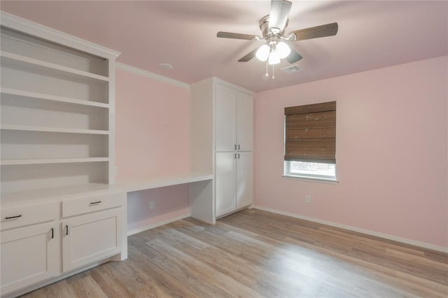 unfurnished bedroom featuring ceiling fan, visible vents, built in desk, baseboards, and light wood-style flooring