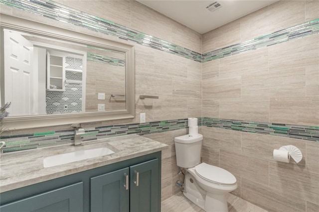 bathroom featuring vanity, toilet, tile walls, backsplash, and visible vents