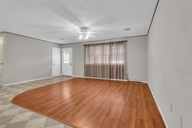 interior space featuring baseboards, visible vents, ceiling fan, and a textured ceiling