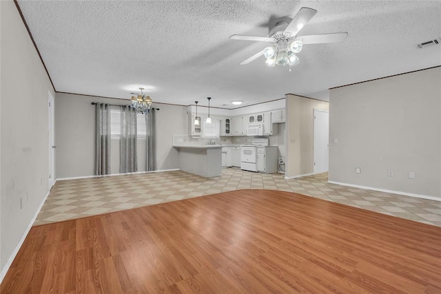 unfurnished living room with a textured ceiling, a sink, visible vents, baseboards, and ceiling fan with notable chandelier