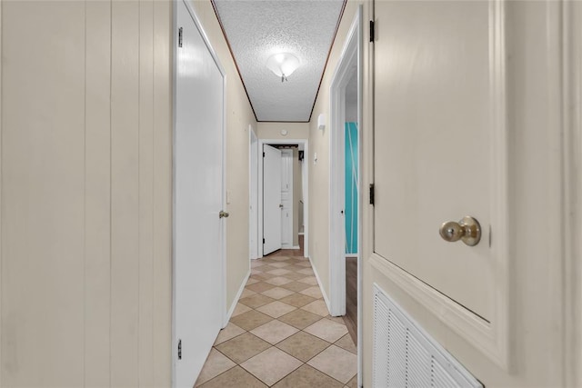 corridor featuring a textured ceiling, visible vents, light tile patterned floors, and baseboards