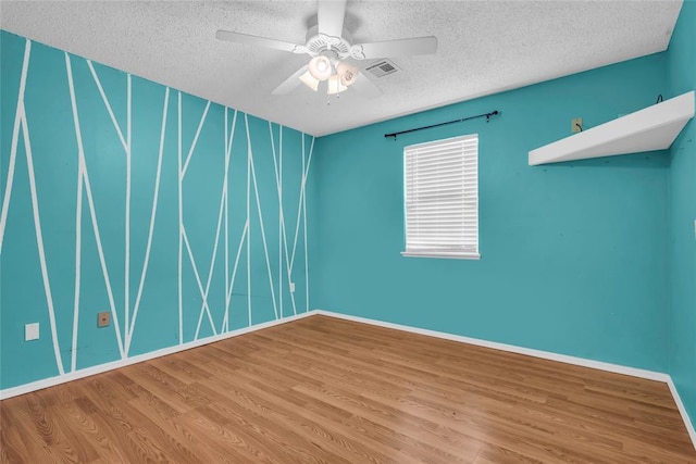 spare room with ceiling fan, a textured ceiling, visible vents, and wood finished floors