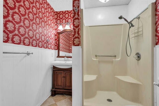 bathroom featuring walk in shower, a textured ceiling, wallpapered walls, and wainscoting