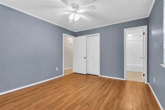 unfurnished bedroom featuring a closet, light wood-type flooring, crown molding, baseboards, and ensuite bathroom