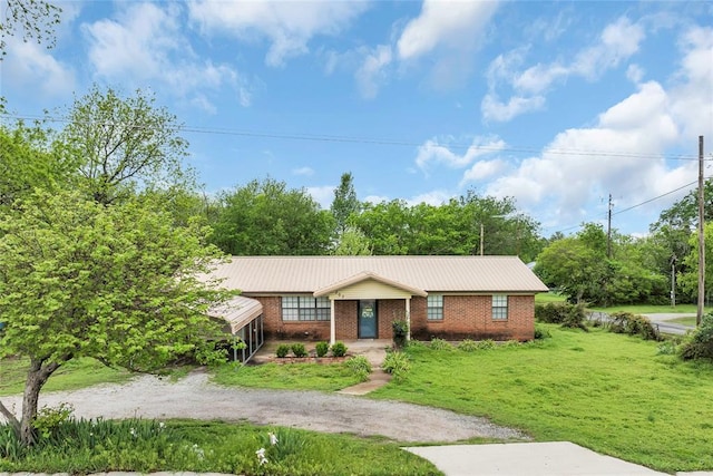 ranch-style home featuring metal roof, a front yard, driveway, and brick siding