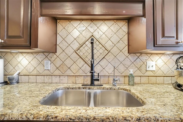 kitchen with backsplash, light stone countertops, and a sink