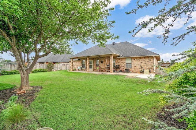 rear view of house with ceiling fan, a patio area, brick siding, a fenced backyard, and a yard