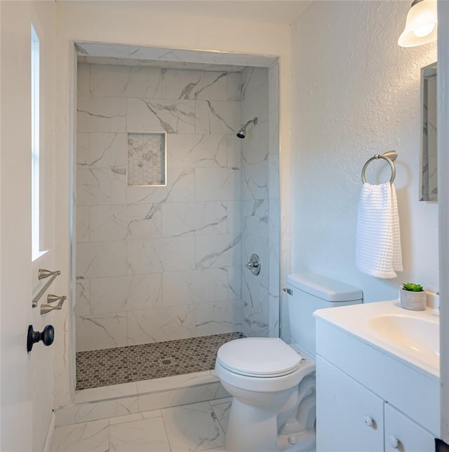 bathroom with a tile shower, a textured wall, toilet, vanity, and marble finish floor