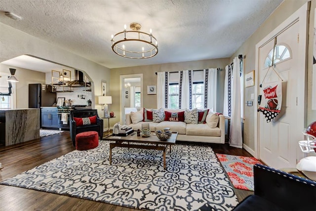 living area with dark wood-style flooring, a textured ceiling, plenty of natural light, and a chandelier