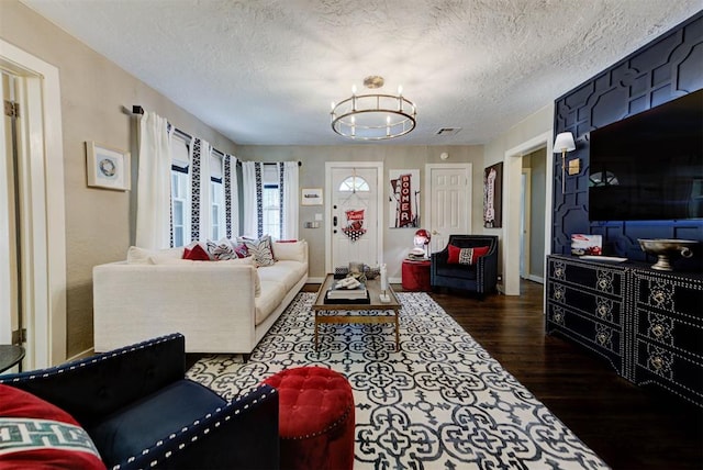 living room featuring a textured ceiling, dark wood-type flooring, visible vents, and a notable chandelier