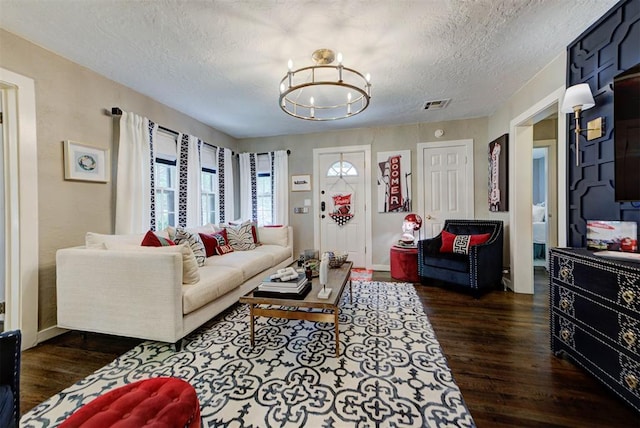 living area featuring an inviting chandelier, a textured ceiling, visible vents, baseboards, and dark wood-type flooring